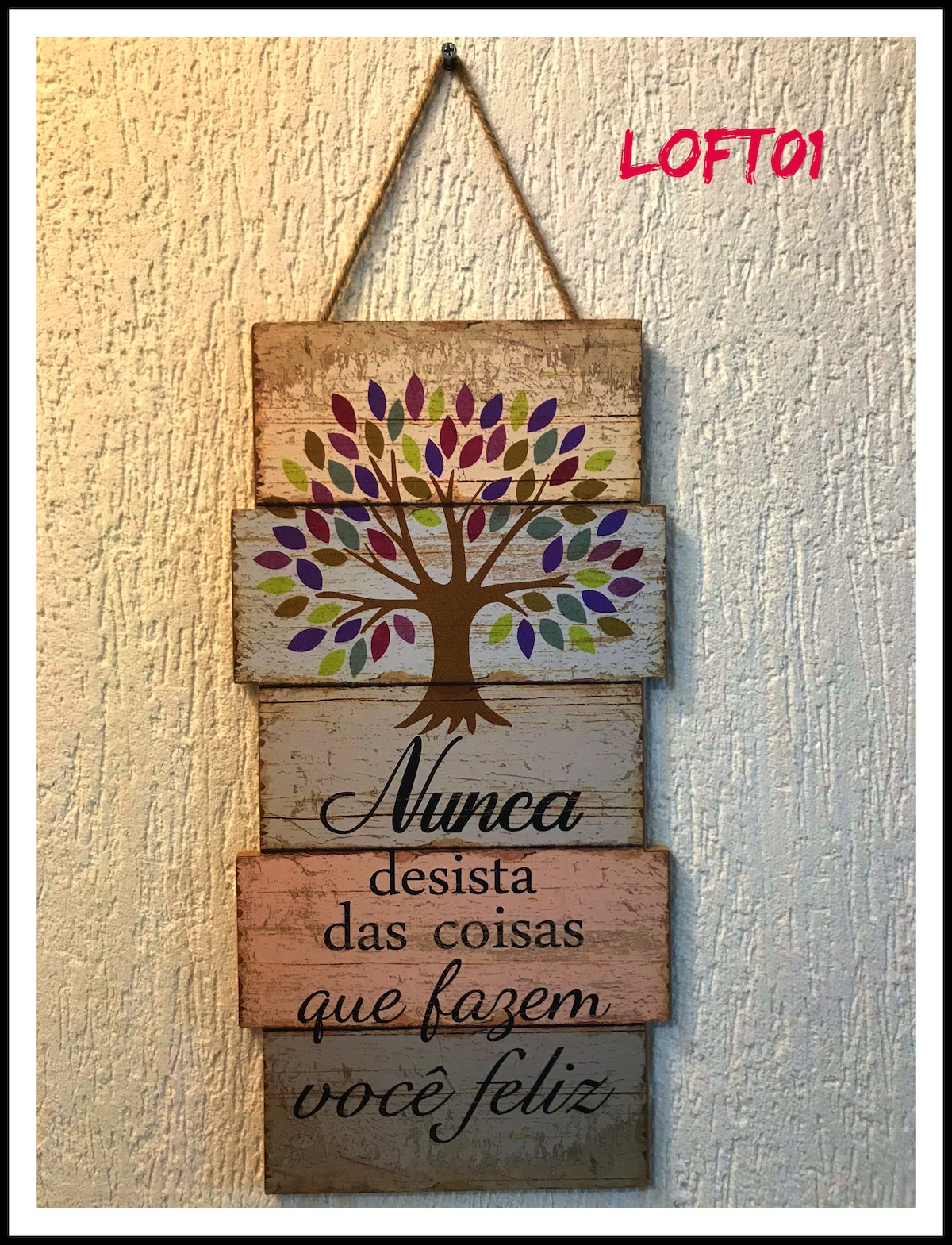 A decorative wooden wall sign is displayed, featuring a colorful tree design. The text translates to 'Never give up on the things that make you happy.' The sign is mounted on a textured light-colored wall, adding a personal touch to the space.