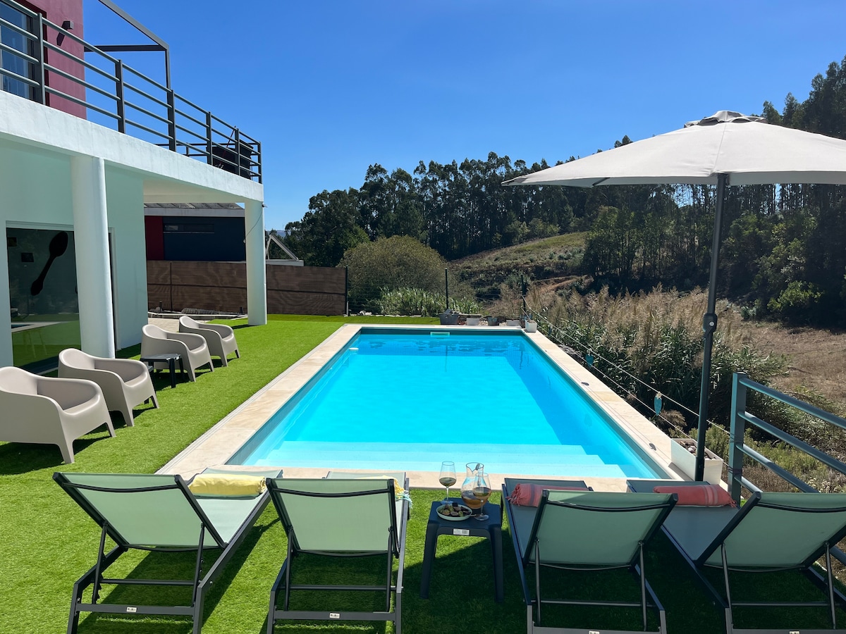 A private pool is surrounded by lounge chairs on a green lawn, offering a view of the scenic valley. A large umbrella provides shade next to the pool, enhancing the space for relaxation and outdoor enjoyment.