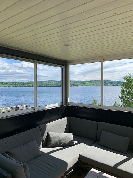 A cozy seating area features a grey sectional sofa with soft cushions, providing comfort and relaxation. Expansive windows frame a panoramic view of the lake and surrounding greenery, inviting in natural light and enhancing the serene atmosphere.