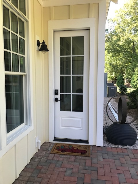 The entrance features a white door framed by six glass panels, providing a connection to the outdoors. A welcoming mat lies at the base, while a decorative sculpture and a stone pathway enhance the inviting ambiance of the entryway.