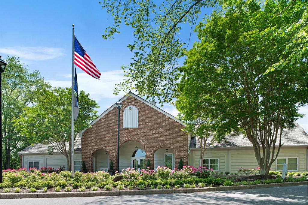 The entrance of the resort features a charming brick building with arched doorways, surrounded by well-maintained gardens filled with colorful flowers. A flagpole displays the American flag against a clear blue sky, adding a sense of welcoming atmosphere.