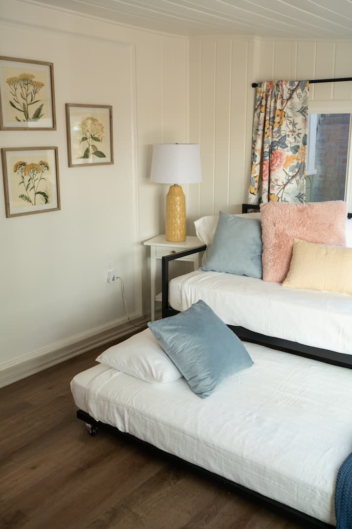 The Sunshine Room. ნათელი პატარა სივრცე ორადგილიანი საწოლითა და დასაწოლი საწოლით.