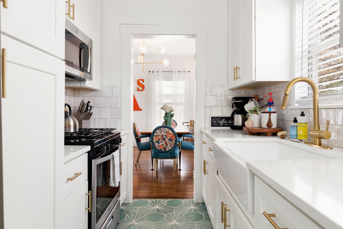 A well-equipped kitchen is showcased, featuring stainless steel appliances, including a gas stove and oven. The countertops are complemented by a decorative backsplash, while a view of the adjacent living area is visible through an open doorway. Soft natural light is filtered through the window.