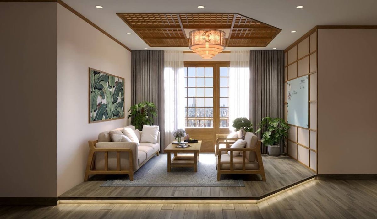 An inviting living area features a light-toned wood coffee table surrounded by a sofa and two armchairs. Floor-to-ceiling windows allow natural light to illuminate the space, which is complemented by wooden accents and indoor plants. A modern light fixture adds a warm ambiance.