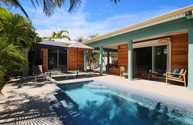 A spacious outdoor area is showcased, featuring a private swimming pool surrounded by tropical plants. Comfortable seating arrangements and two umbrellas provide shade, while the adjacent covered terrace offers additional seating, creating an inviting space for relaxation and enjoyment.