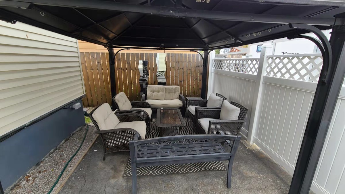 A shaded outdoor seating area features a selection of comfortable chairs and a central coffee table. The space is enclosed by wooden fencing, providing privacy. Lattice panels add an aesthetic touch, while a patio surface enhances outdoor relaxation.