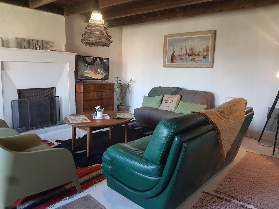 A living room features a green leather sofa and two light green chairs, arranged around a wooden coffee table. A rug adds warmth to the space, while a vintage painting hangs above the mantel. Natural light illuminates the area, highlighting a cozy atmosphere.