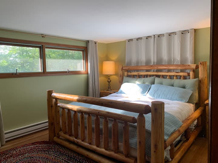 Chambre principale avec lit king size rustique en rondins et rideaux obscurcissants. Table d'appoint, chargeurs de téléphone, réveil, placard avec cintres pour vos effets personnels ainsi qu'une commode pour vos vêtements.