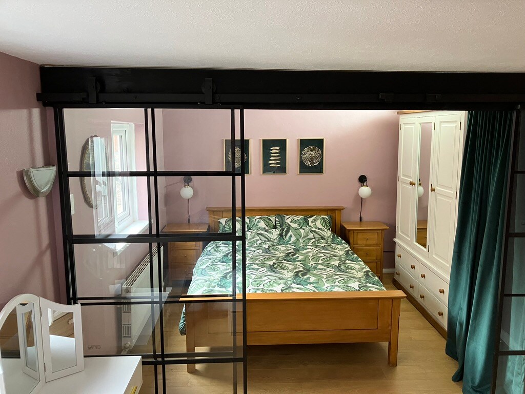 Cama tamaño king en una habitación que tiene puertas correderas y una cortina de longitud de piso para un poco de paz y privacidad.