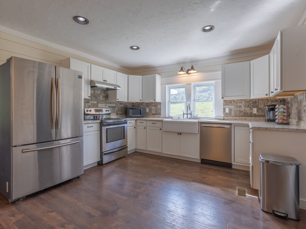 The updated kitchen features a stainless steel refrigerator and stove alongside white cabinets. A sink is positioned beneath a window, allowing natural light to illuminate the space. Countertops offer ample workspace, and a modern dishwasher is also present, enhancing convenience.