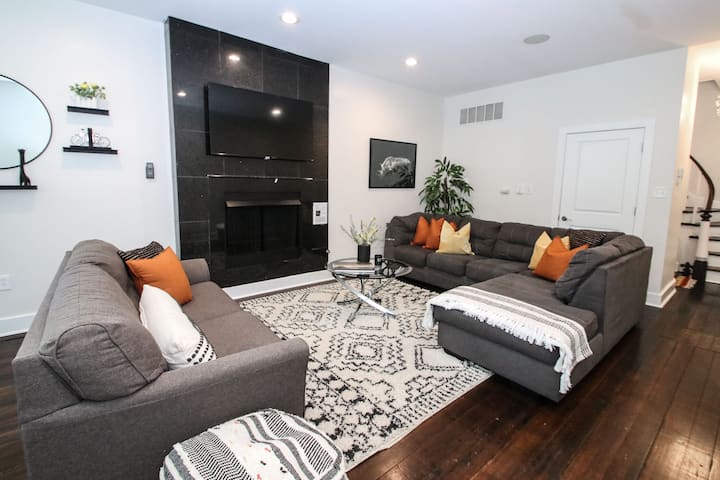 אח מודרנית, ספות אפורות מסוגננות וכריות בגוון חם יוצרים אווירה מסבירת פנים.