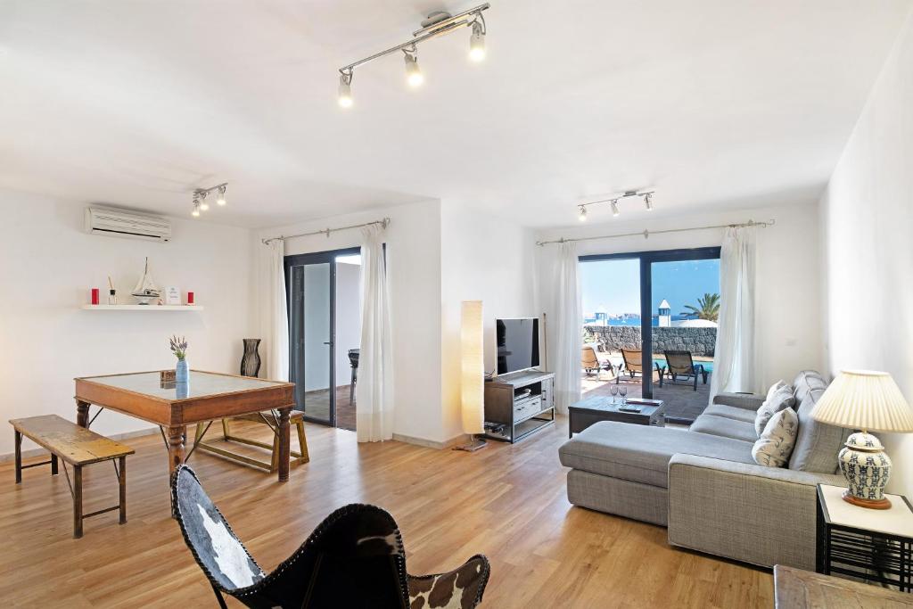 A spacious living and dining area is highlighted by large windows offering views of the terrace and the sea. A comfortable sofa sits adjacent to a sleek entertainment center, while a wooden dining table provides ample seating. Neutral tones create a bright, inviting ambiance.