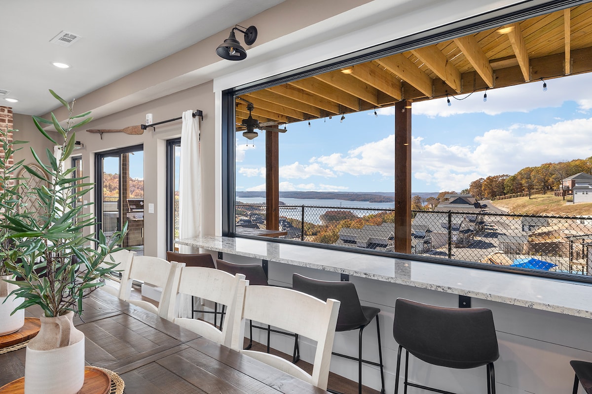 A spacious dining area features a large wooden table surrounded by several chairs, with a window offering a clear view of the outdoor patio and serene lake. The sliding doors provide easy access to the outdoor space, enhancing the open-concept design.