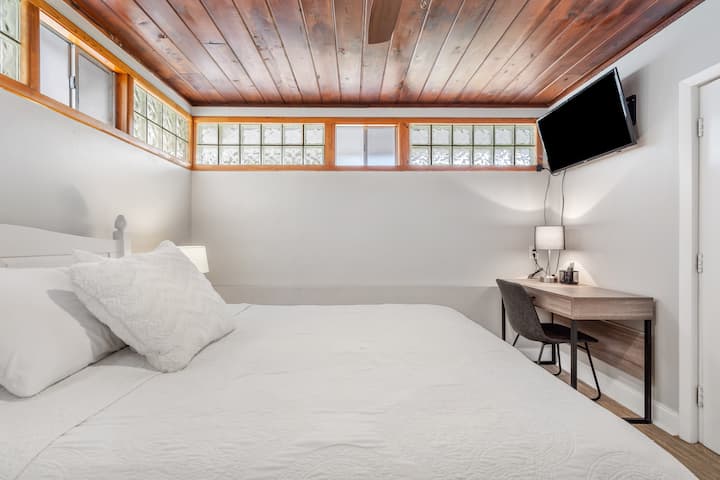 Master bedroom with a queen size bed, mounted TV and a desk.