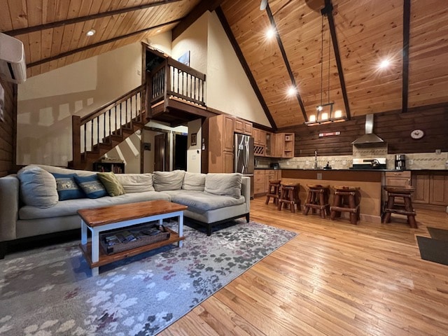 An open living space features a light-colored sectional sofa arranged around a wooden coffee table on a patterned rug, with a vaulted wood ceiling overhead. A well-equipped kitchen is visible in the background, complemented by a dining area with wooden stools.