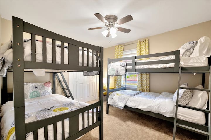 غرفة بطابقين تضم سريرين مزدوجين فوق سريرين صغيرين ولعب أطفال وكتب 