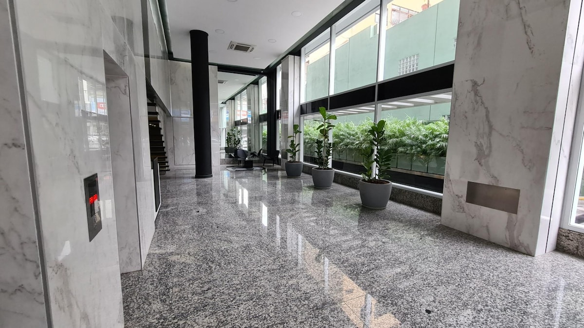 A spacious lobby area is highlighted by polished marble flooring and large windows that allow ample natural light. Potted greenery adds a touch of nature, while the elevator is easily accessible. Seating areas provide a comfortable space for relaxation.