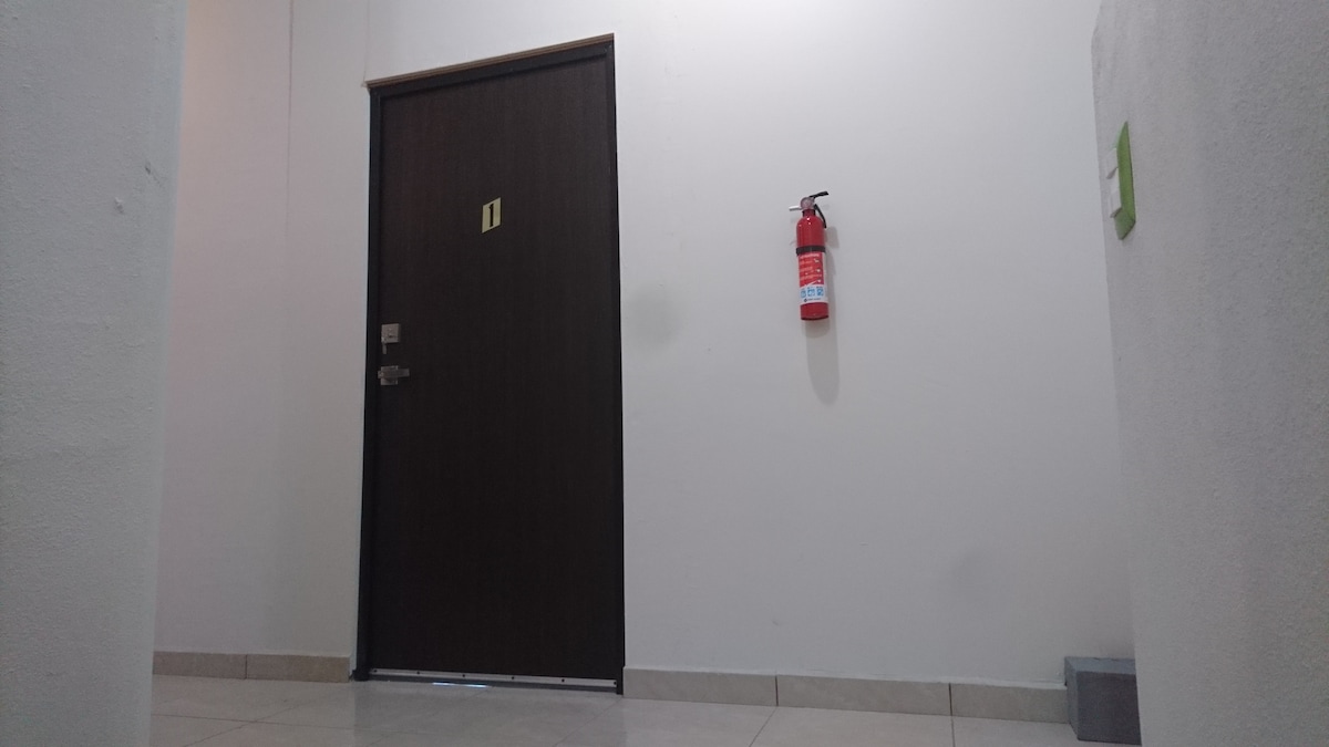 A corridor is presented, featuring a dark wood door marked with the number 1. A fire extinguisher is mounted on the wall next to the door. The floor is tiled, and neutral-colored walls provide a simple backdrop.