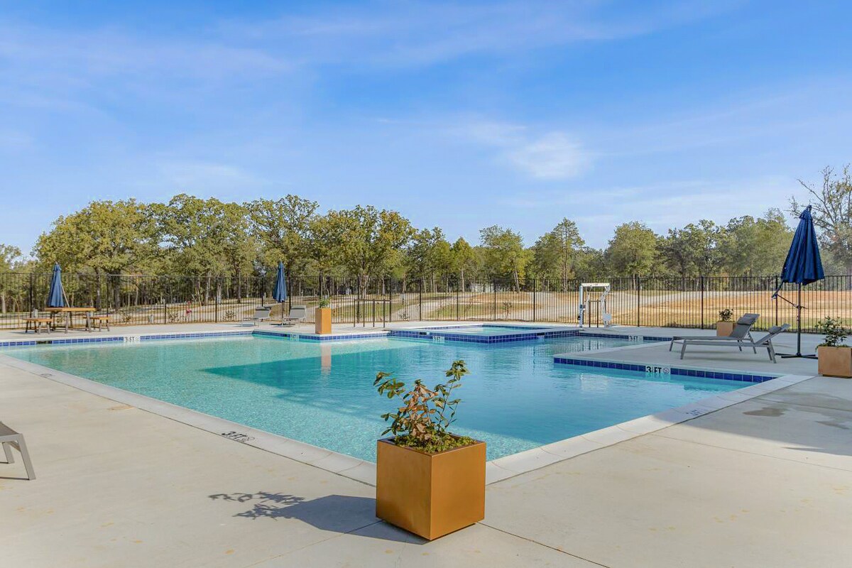 An outdoor swimming pool is presented, featuring a spacious area with lounge chairs and umbrellas. Surrounding greenery is visible, along with a minimalistic aesthetic enhanced by potted plants at the edge. A shallow area is included for easy access.