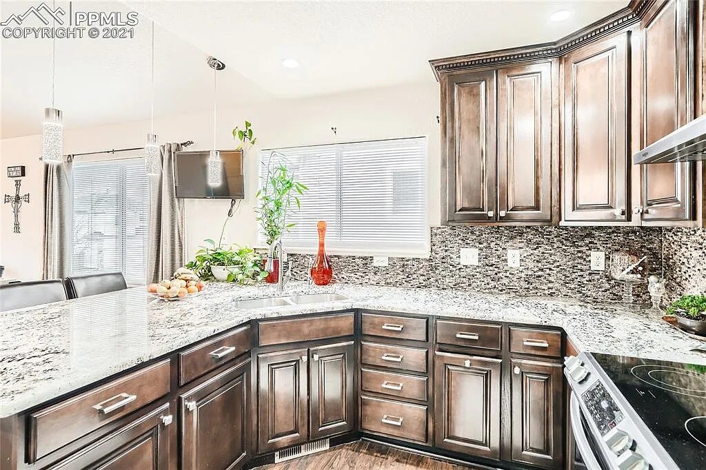 A modern kitchen is showcased with dark wood cabinetry and a sleek granite countertop. Natural light illuminates the space through a window. An arrangement of plants adds a touch of greenery, and a variety of kitchen utensils and appliances are neatly arranged.
