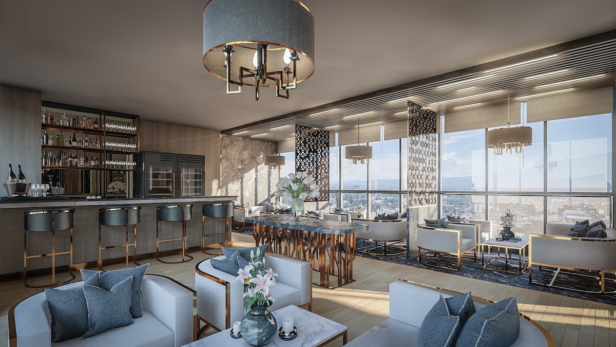 A modern living space features large windows providing panoramic city views. A bar area is visible with high stools, while a dining table occupies the center of the room. Comfortable seating arrangements are accompanied by decorative accents, including vases and cushions. Soft lighting enhances the sophisticated ambiance.