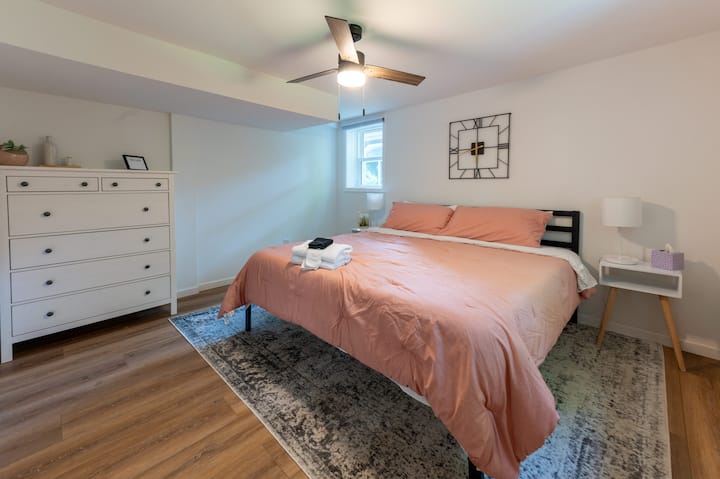 Piate spálňa na spodnom poschodí má manželskú posteľ, komodu, skriňu, nočné stolíky, lampy, zatemňovacie žalúzie a stropný ventilátor.