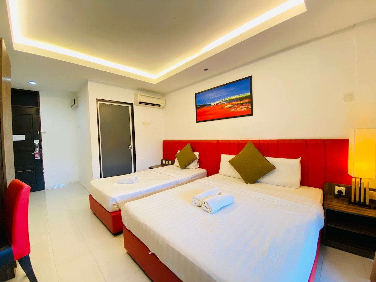 A well-lit guest room features two spacious beds, each adorned with decorative pillows. A vibrant piece of wall art adds color above the beds, while soft recessed lighting enhances the modern decor. A seating area with a chair and desk is positioned nearby.