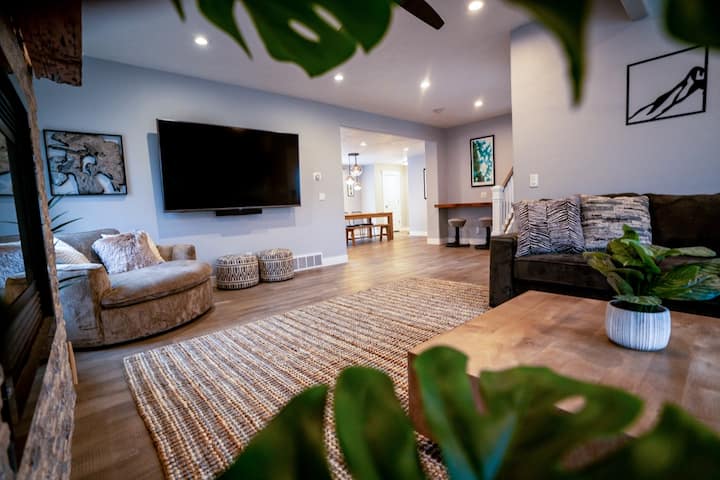 Მისაღები ოთახი 85"-იანი სმარტ-ტელევიზორით, Sonos ხმის ზოლით, უზარმაზარი სექციური სკამითა და ბუხრით. 