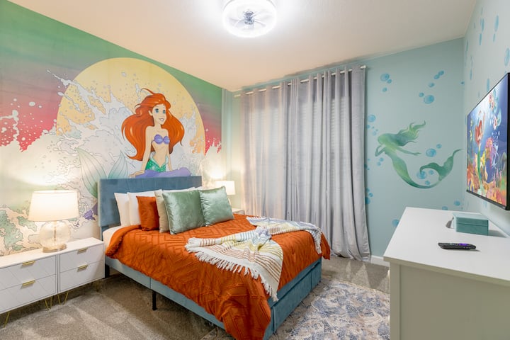 Immergiti nei sogni della Sirenetta: un soffitto blu oceano imita le onde dolci, letti gemelli fiancheggiano un grande murale di Ariel, tende turchesi si gonfiano come schiuma di mare, accenti di vimini evocano barriere coralline tropicali e l'illuminazione ispirata alle conchiglie proietta un caldo bagliore sul mare.  