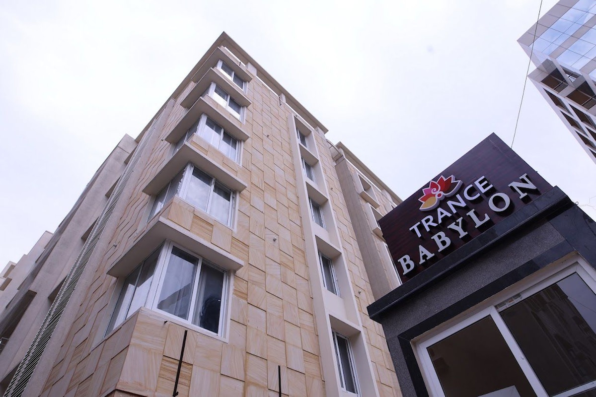 The exterior view of a multi-story building is displayed, featuring a modern design with light-colored stone cladding. Prominently featured at the base is a sign for 'Trance Babylon', with large windows visible on each floor.