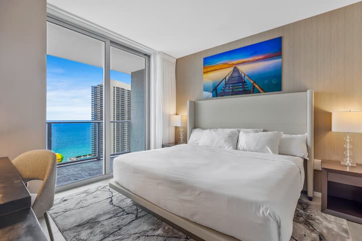 Შეაბიჯეთ მთავარ საძინებელში, სადაც დიდი ზომის საწოლი, რბილი განათება და თანამედროვე დეკორი მშვიდი დასვენების საშუალებას იძლევა. Იატაკიდან ჭერამდე ფანჯრები ღიაა აივანზე, საიდანაც ოკეანის ხედი იშლება, ცალკე სააბაზანო კი კომფორტსა და კომფორტს ქმნის.