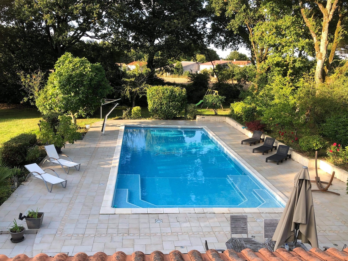 A private swimming pool is situated within a spacious outdoor area, surrounded by well-maintained greenery. Sun loungers are positioned around the pool deck, providing ample space for relaxation. A shaded seating area is visible to one side, allowing for comfortable enjoyment of the outdoor setting.