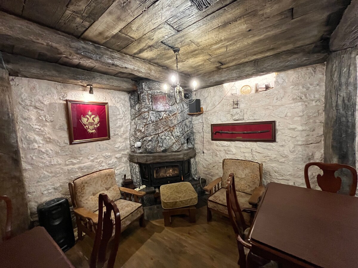 A rustic corner of the living area features a stone fireplace framed by two upholstered chairs and a wooden table. The walls are adorned with decorative elements and artwork, providing a cozy ambiance in this earthy space.