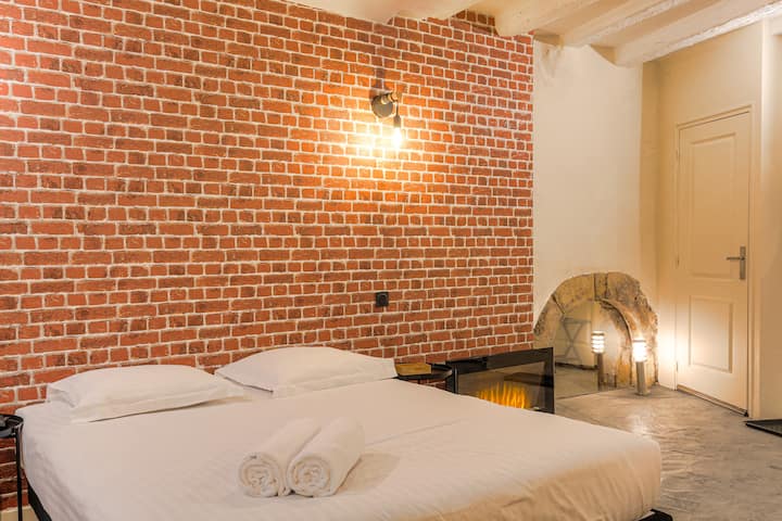 Zona de dormitorio con cama doble, ropa de cama de hotel y pared de ladrillo