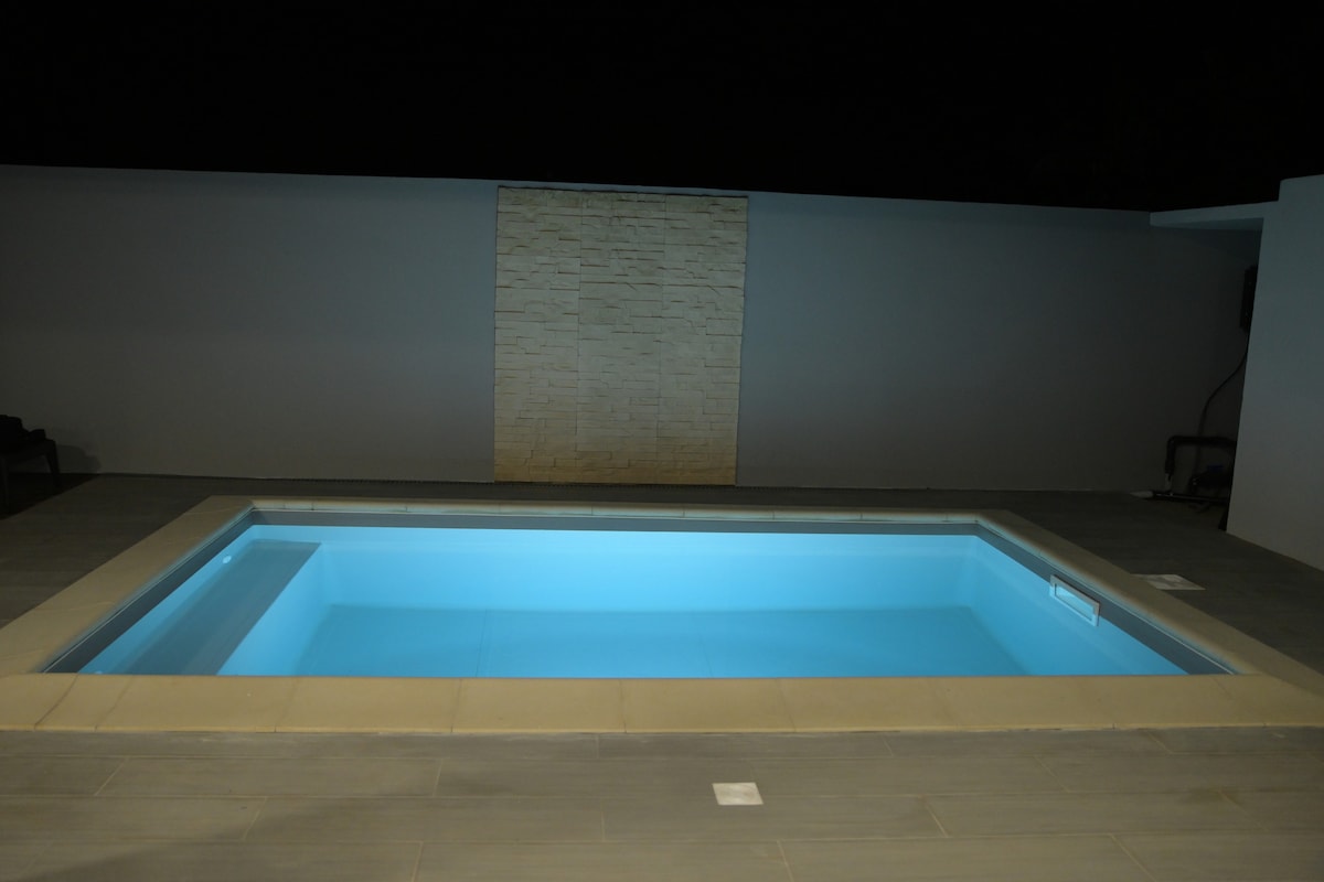 A private heated pool glows softly under the night sky, featuring clear blue water and smooth tile surroundings. A stone wall backdrop adds a subtle texture, contributing to a serene outdoor atmosphere.