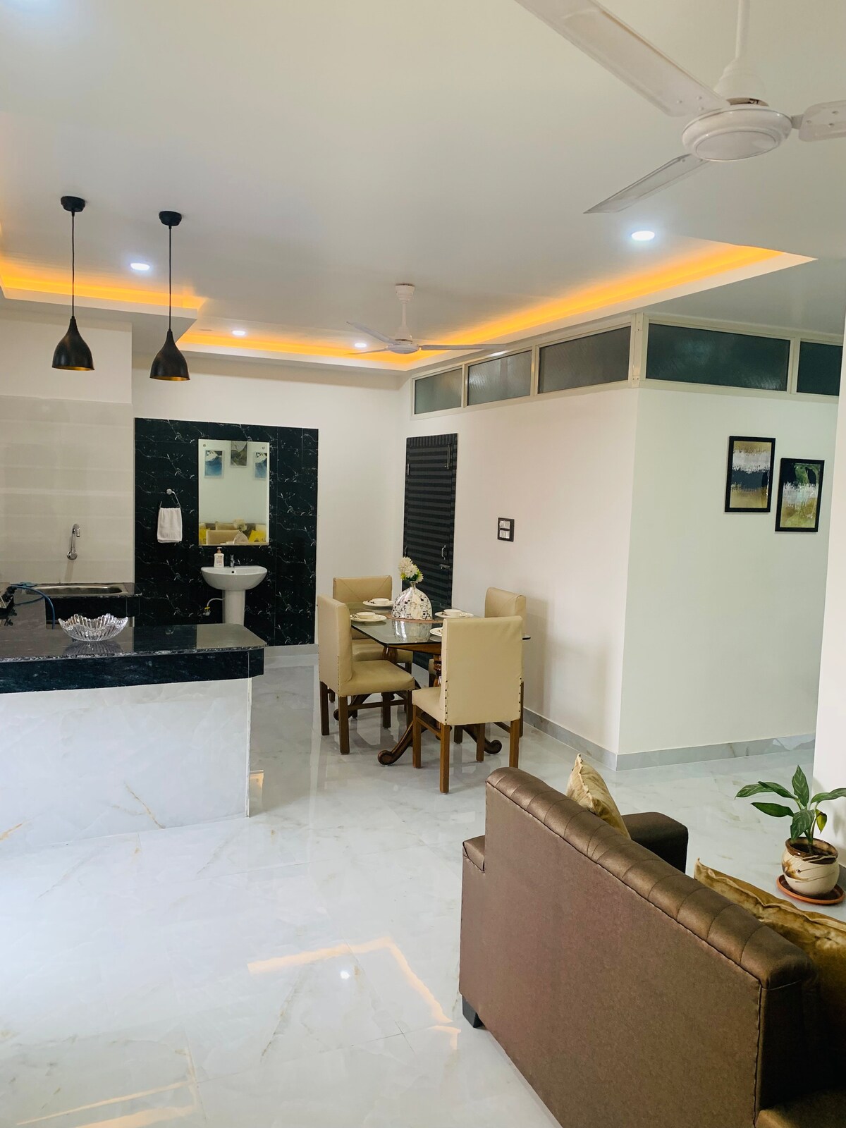 The interior space features a modern dining area with a wooden table and beige chairs. A stylish kitchen island with dark countertops is situated nearby. Soft lighting highlights the room, complemented by a minimalist sofa and a potted plant in the corner.