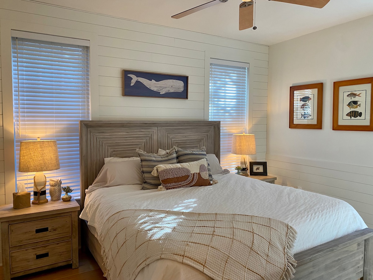 بياضات القطن الفاخرة والأثاث الخشبي القديم والشمس في وقت متأخر من اليوم تجعل غرفة النوم الرئيسية هذه رحلة ترحيبية في نهاية يوم طويل