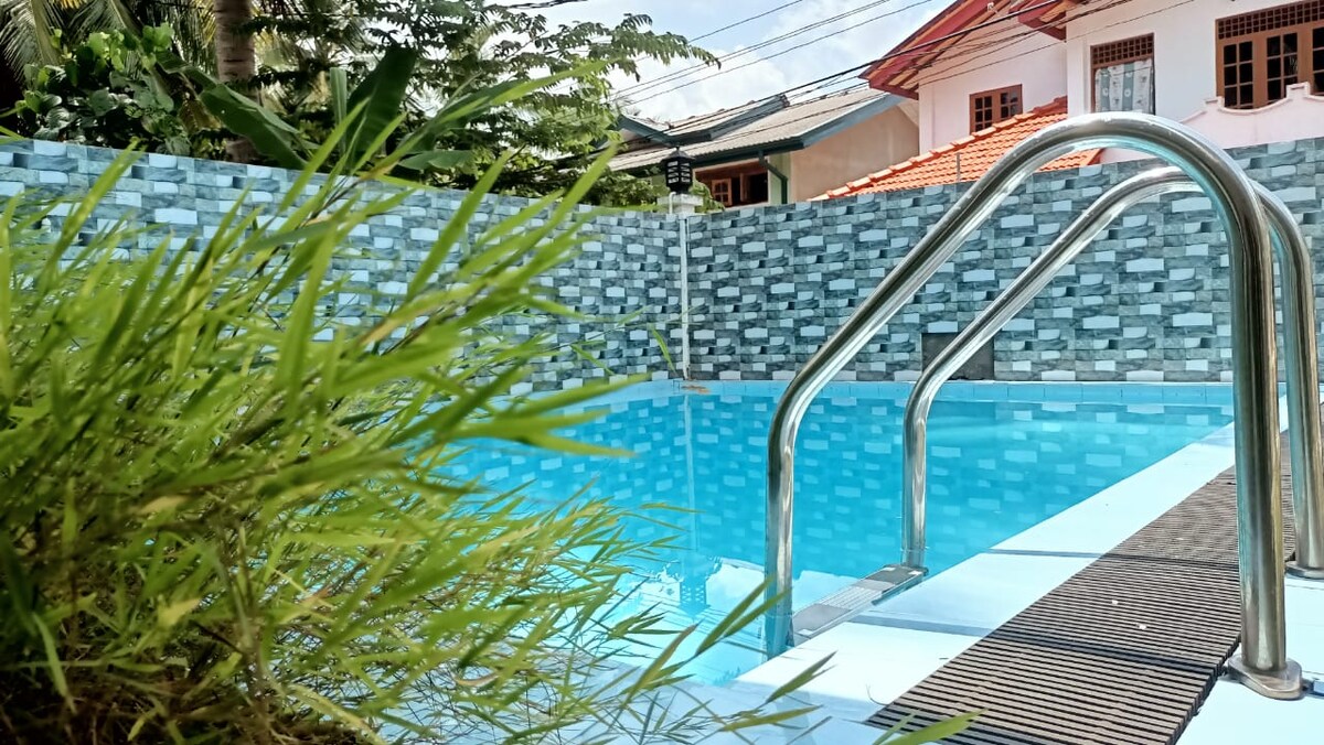 A clean pool is surrounded by textured blue and grey tiles, creating a refreshing ambiance. Lush green grass gently frames the pool's edge, adding a touch of nature. The clarity of the water invites relaxation under the sunlight.