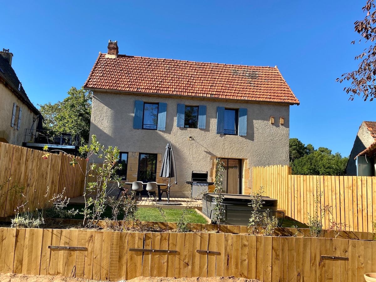 A spacious two-story house is depicted, featuring a red-tiled roof and multiple blue windows. A fenced garden includes a shaded seating area with chairs, a wooden table, and a spa. Clear blue skies complement the serene outdoor setting.