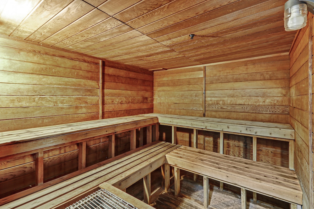 A wooden sauna is shown, featuring simple bench seating arranged along the walls. The interior is lined with wooden panels, creating a warm and inviting space. Soft lighting is provided by a single overhead fixture, enhancing the calming atmosphere in this private wellness area.