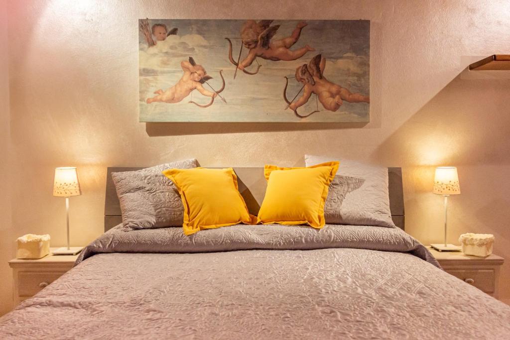 A cozy bedroom is presented with a spacious bed adorned with a light grey coverlet and yellow accent pillows. Soft lighting is provided by two bedside lamps. A mural of cherubic figures is displayed above the headboard, adding character to the room.
