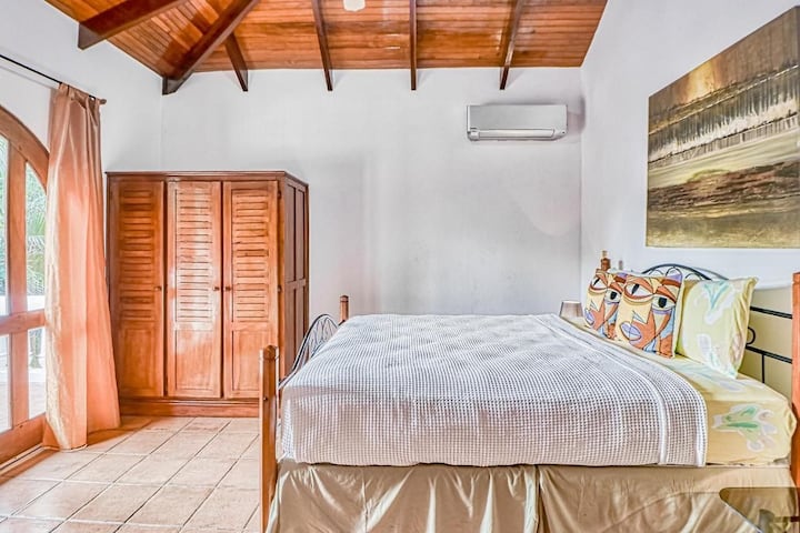 Segundo dormitorio delantero con cama tamaño queen y amplio espacio en el armario con puerta con arco hacia la amplia terraza/balcón de la casa con vistas a la piscina y a los jardines hacia la playa.