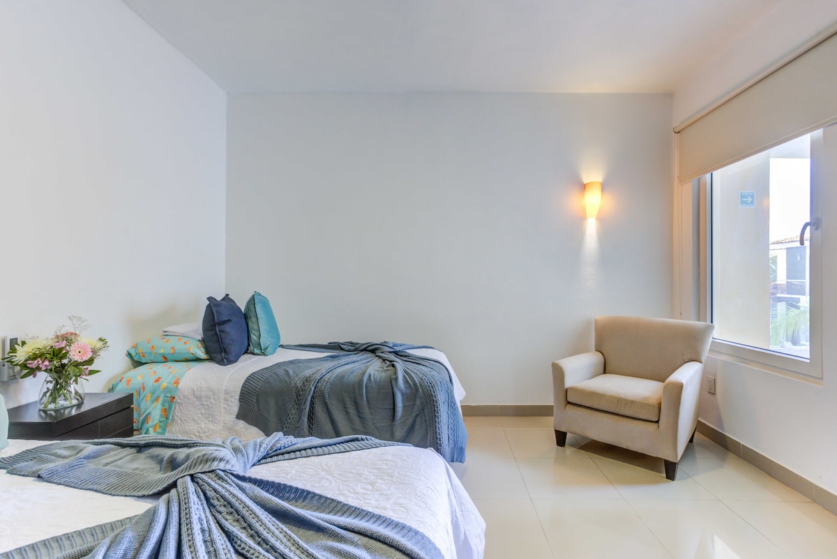 تحتوي غرفة النوم الثانية على سريرين مفردين وكرسي بذراعين