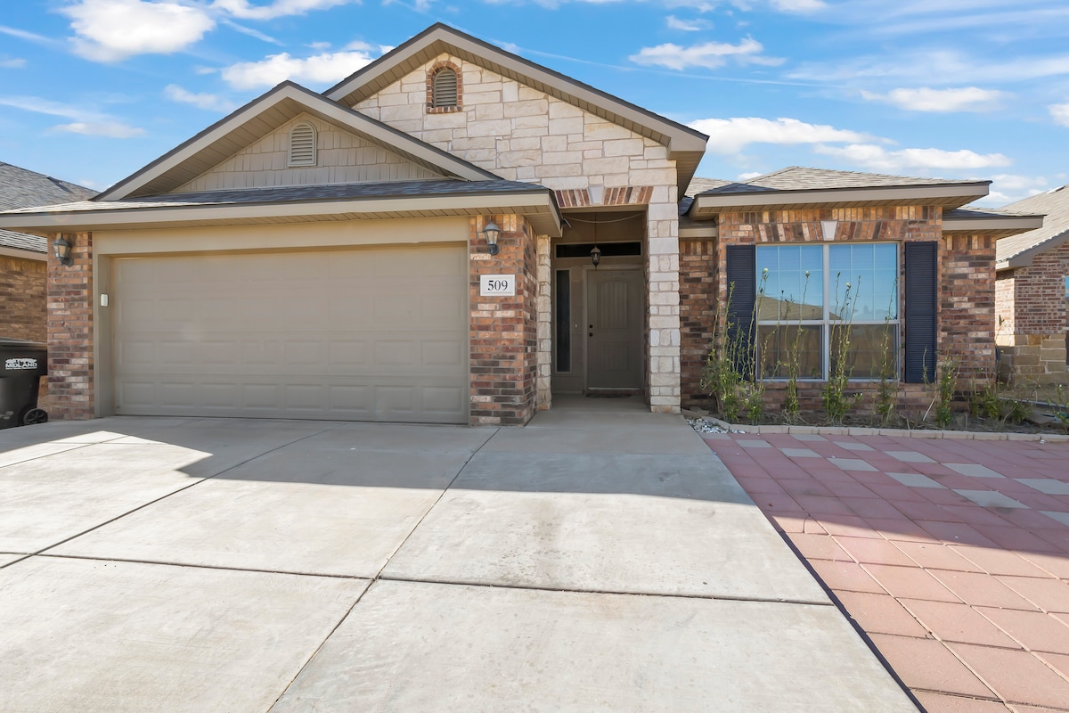 A single-story home features a combination of brick and stone exterior, with a neatly paved driveway leading to a two-car garage. The entrance is framed by a welcoming porch, and the front yard includes minimal landscaping and a pathway leading to the entrance.