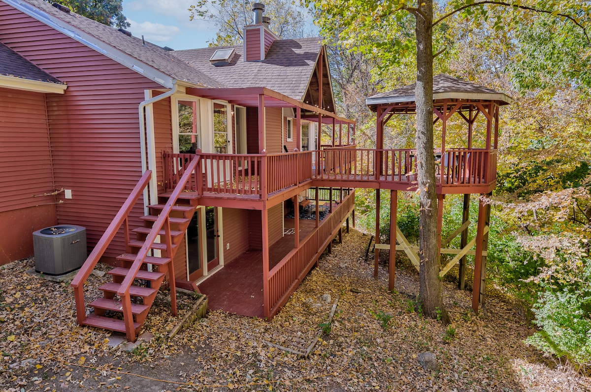 The exterior of the home features a wooden deck that connects to a gazebo nestled among the trees. Sturdy steps lead up to the elevated deck area, surrounded by autumn leaves, creating a serene outdoor setting.