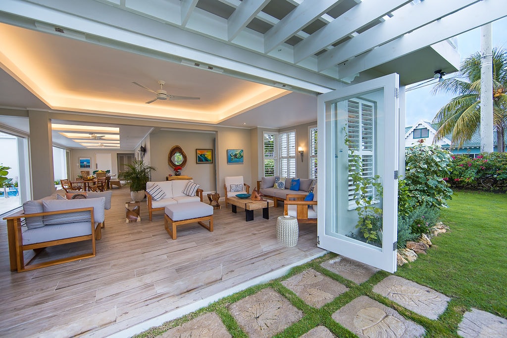 An open living space is shown, featuring comfortable seating arranged around a central coffee table. Large glass doors provide a seamless transition to the outdoor area. Natural light fills the room, highlighting the modern decor and lush greenery visible outside.
