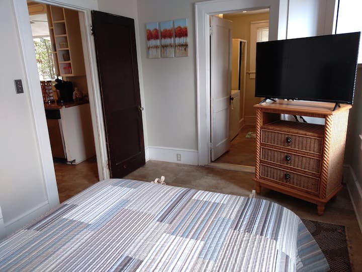 Dormitorio completo, que muestra la puerta abierta a la cocina y la puerta abierta al medio baño privado, con lavadora y secadora. Actualmente no hay TV en esta ubicación.