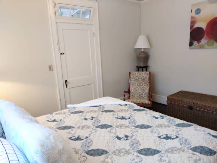 Dormitorio tamaño king que muestra la puerta cerrada con llave a la habitación del porche trasero, la mecedora y el baúl de almacenamiento de ropa de cama.