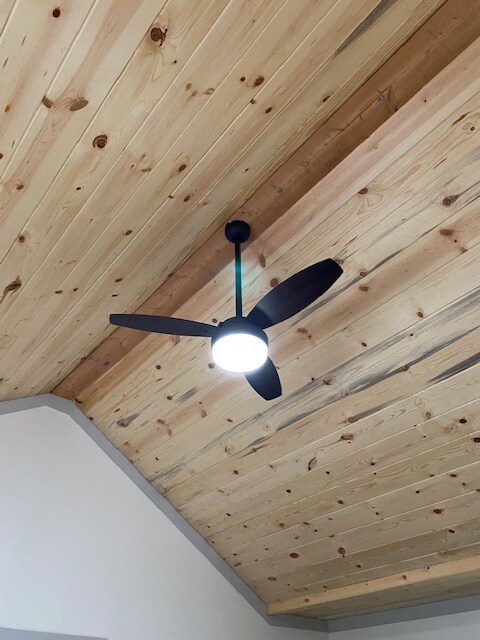 A ceiling fan with three blades is situated in the center of the room, featuring an integrated light fixture below. The ceiling is adorned with natural wood planks, showcasing a warm tone and a smooth finish.