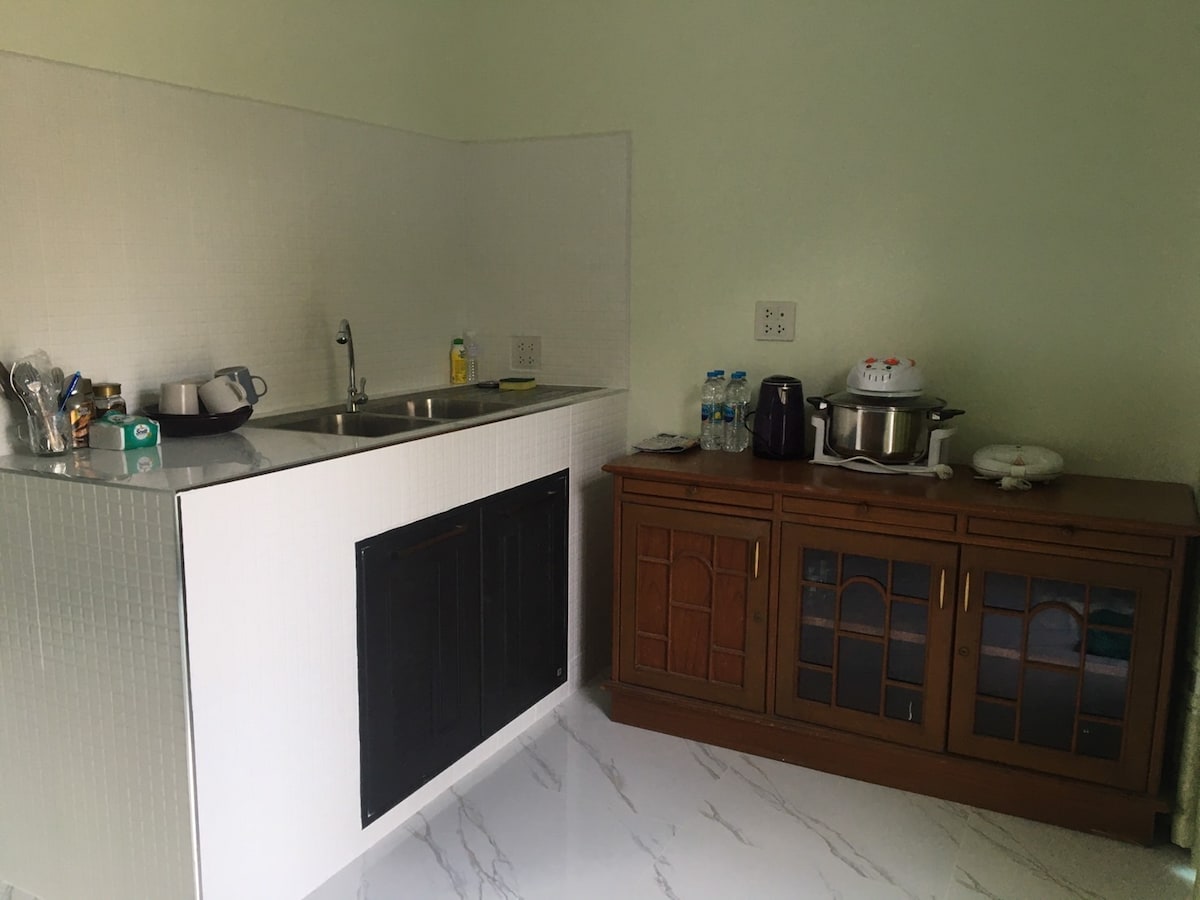 A well-equipped kitchen area features a stainless steel sink and a two-burner stove. An adjacent wooden cabinet maximizes storage, with various utensils and appliances visible. The glossy marble floor enhances the space's bright and clean appearance.